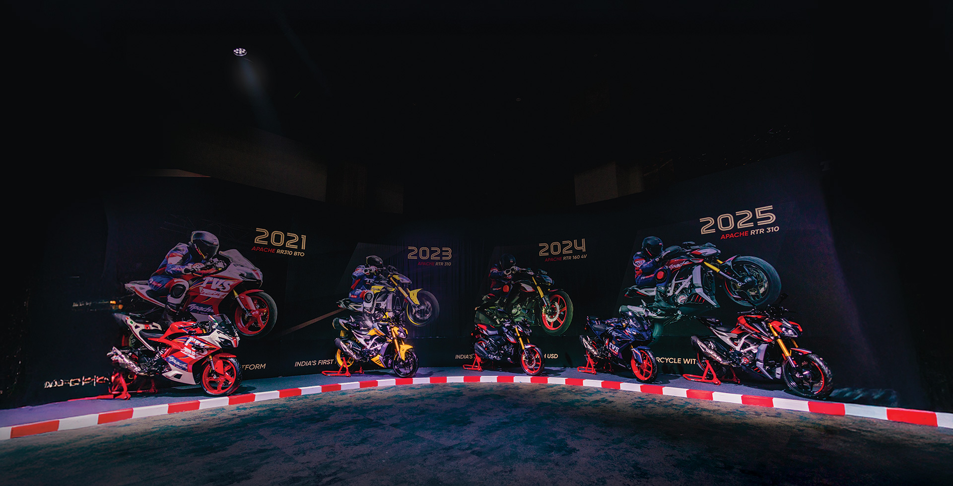 Two decades of TVS Apache motorcycles lined up on a race stage &mdash; from the 2021 Apache RR 310 to the 2025 Apache RTR 310
